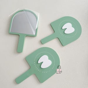Puede incluir: Tres espejos de mano y paletas de tem&aacute;tica dental de color verde menta. Un espejo tiene una pel&iacute;cula protectora. Las paletas presentan un gr&aacute;fico de diente blanco y el texto "RESTORE DENTAL". Los art&iacute;culos est&aacute;n dispuestos sobre una superficie blanca.