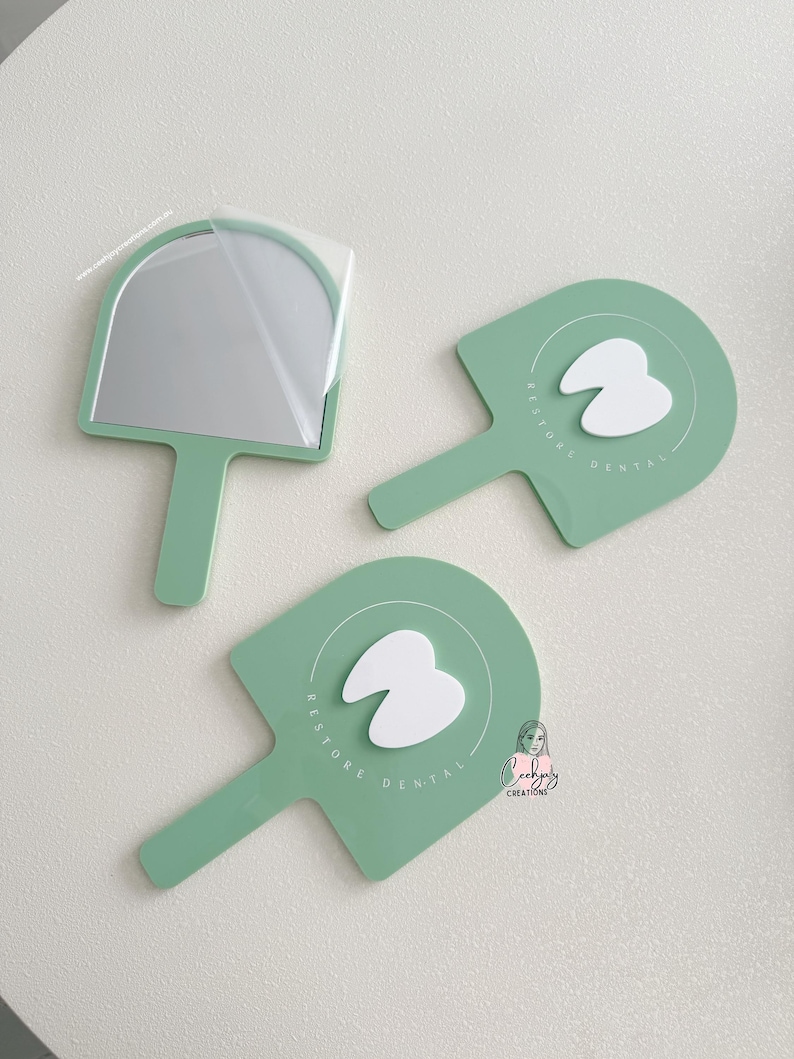 Puede incluir: Tres espejos de mano y paletas de tem&aacute;tica dental de color verde menta. Un espejo tiene una pel&iacute;cula protectora. Las paletas presentan un gr&aacute;fico de diente blanco y el texto "RESTORE DENTAL". Los art&iacute;culos est&aacute;n dispuestos sobre una superficie blanca.