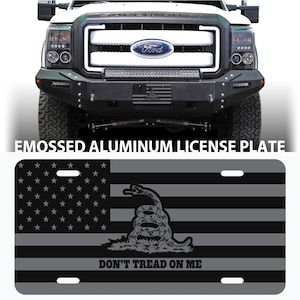 May include: A black and gray aluminum license plate with an American flag and a coiled snake with the words "Don't Tread On Me".