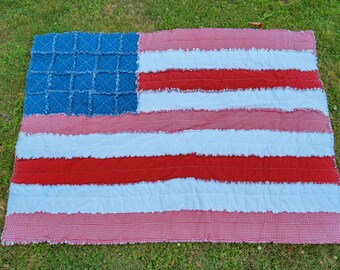 May include: A rectangular rag quilt designed to resemble the American flag. The quilt features a blue square section with a grid pattern and alternating horizontal stripes in red and white, all constructed with frayed fabric edges throughout.