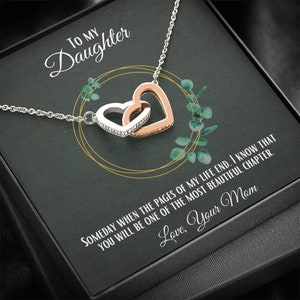 Op de afbeelding: Een zilveren ketting met twee in elkaar grijpende hart hangers, een zilveren en een roségouden. De ketting wordt geleverd in een zwarte doos met een boodschap aan een dochter die luidt: "Op een dag, wanneer de pagina's van mijn leven eindigen, weet ik dat je een van de mooiste hoofdstukken zult zijn. Liefs, Mama."