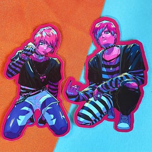 以下が含まれることがあります： パンク風の衣装を着た人物のイラストが描かれたステッカー2枚。人物は、鮮やかなピンク、ブルー、ブラックのアクセントで、カラフルでスタイリッシュな方法で描かれています。ステッカーはピンクとブルーの背景に貼られています。