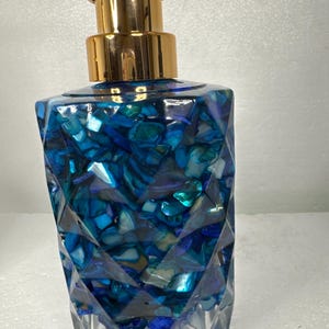 May include: A blue and gold soap dispenser with a geometric design. The dispenser is filled with blue and white iridescent pieces.