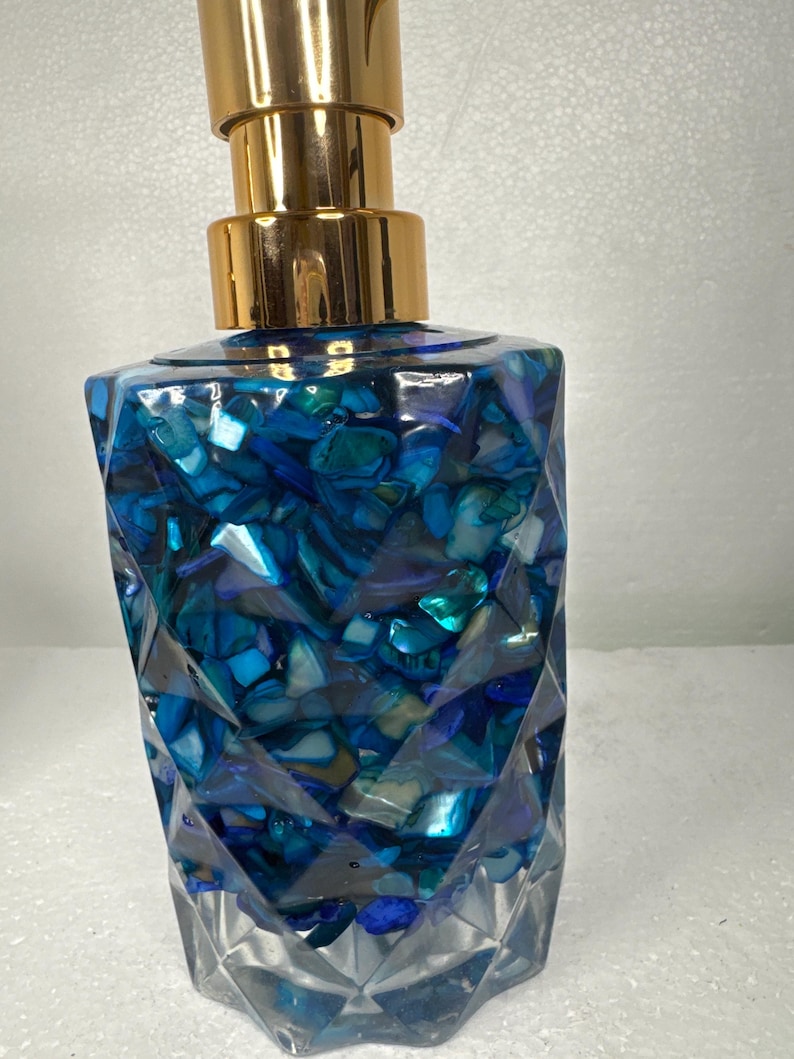 May include: A blue and gold soap dispenser with a geometric design. The dispenser is filled with blue and white iridescent pieces.