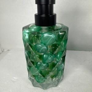 May include: A green glass soap dispenser with a black pump. The dispenser is filled with green stones and has a faceted design.