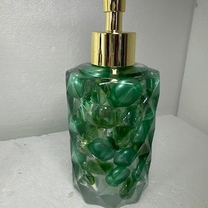 May include: A green glass soap dispenser with a gold pump. The dispenser is filled with green and clear glass stones.