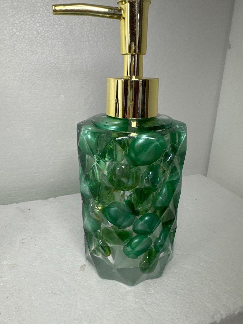 May include: A green glass soap dispenser with a gold pump. The dispenser is filled with green and clear glass stones.