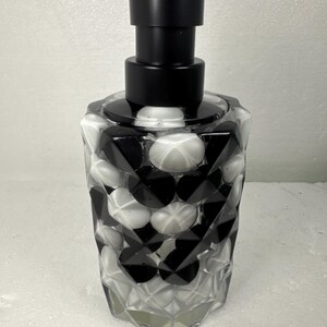 May include: Black and white patterned glass soap dispenser with a black pump. The dispenser has a geometric design.
