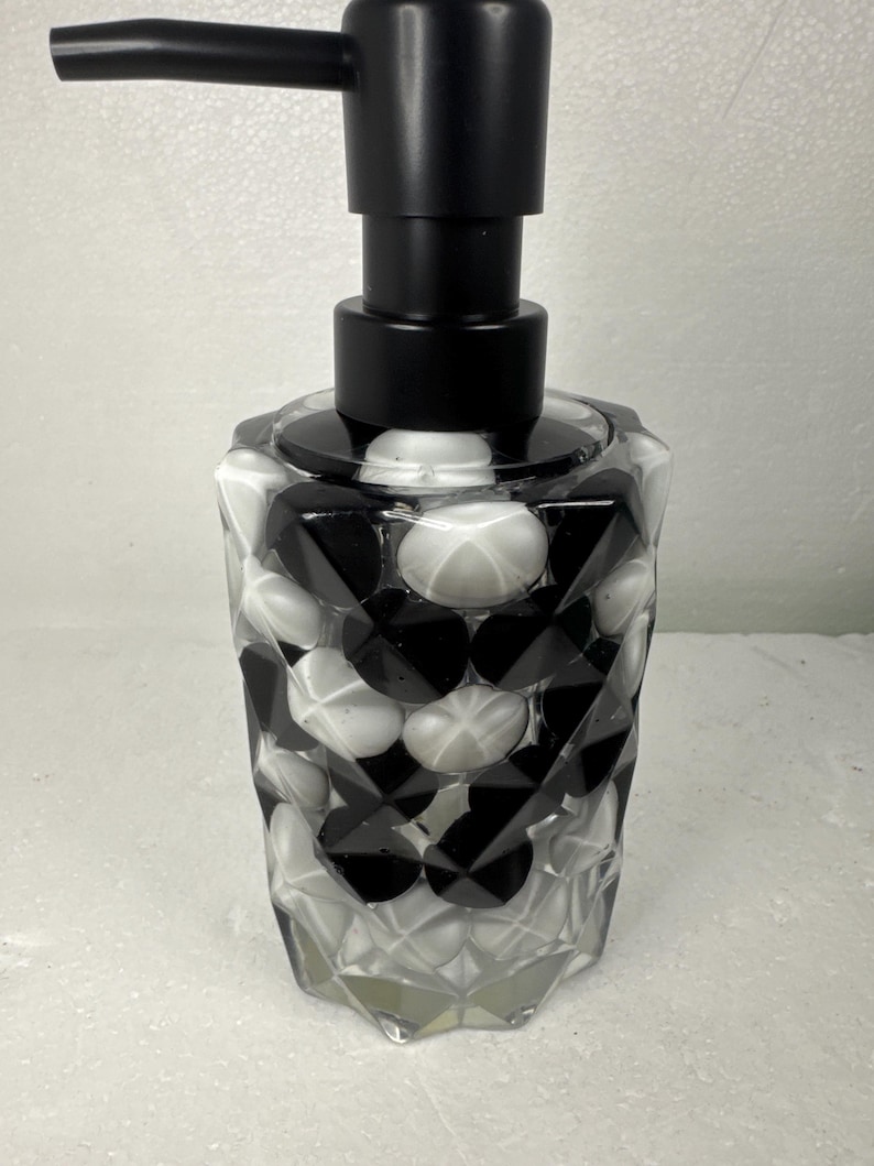 May include: Black and white patterned glass soap dispenser with a black pump. The dispenser has a geometric design.