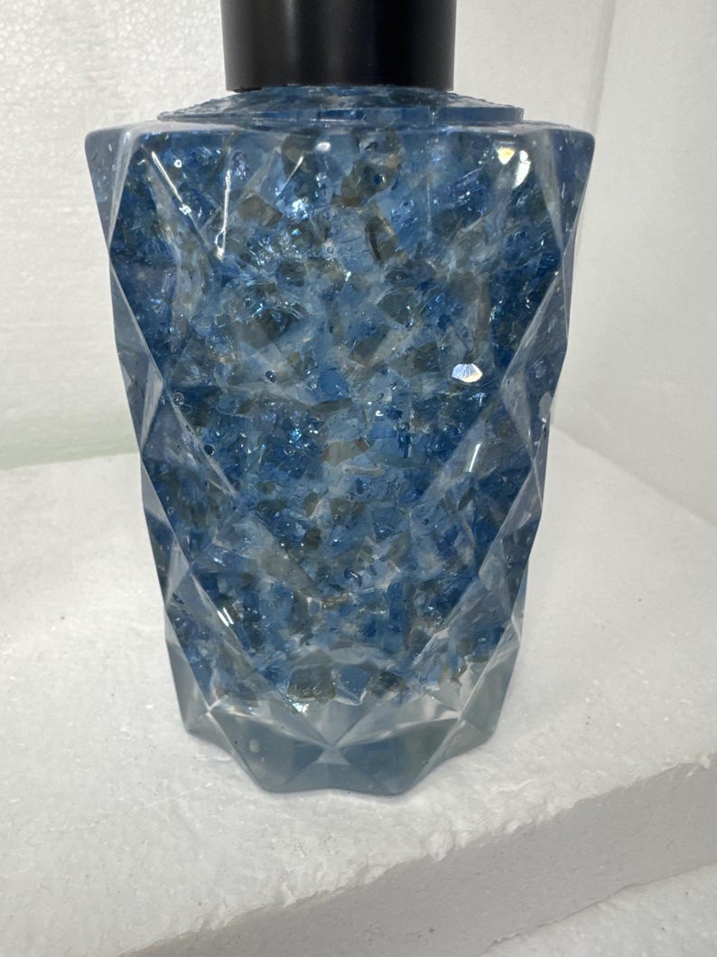 May include: A clear glass bottle with a black pump top. The bottle is filled with blue and white glitter.