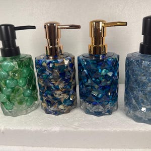 May include: Four decorative soap dispensers with different colored mosaic designs. The dispensers are made of glass and have a gold or black pump.