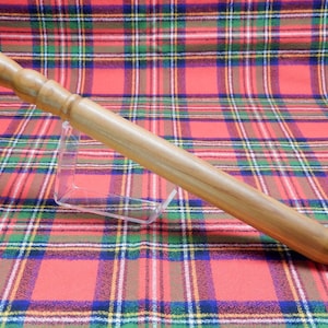 Könnte beinhalten: Eine hellbraune Holzkuchenrolle mit einem abgerundeten Griff und einem sich verjüngenden Körper. Die Kuchenrolle wird auf einem durchsichtigen Kunststoffständer vor einem rot, grün und blau karierten Hintergrund präsentiert.
