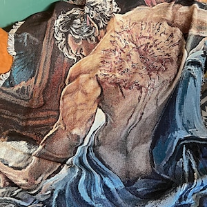 May include: Woven throw blanket depicting a classical male figure in shades of brown, blue, and beige. The blanket has a fringed edge and shows a muscular torso and head with detailed shading.