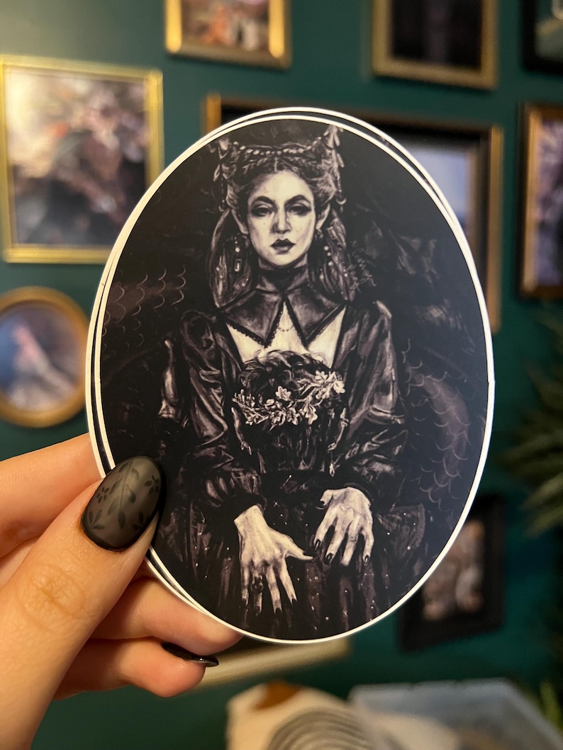 May include: Oval sticker featuring a black and white illustration of a woman in a dark, gothic style dress and crown. The woman has long hair and is holding a bouquet of flowers. The sticker has a white border.