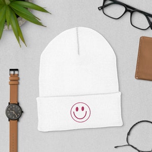 May include: White beanie with a pink smiley face embroidered on the front.