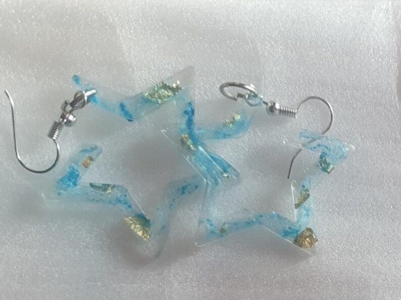 May include: A pair of star-shaped earrings with a clear resin base and blue and gold glitter accents.