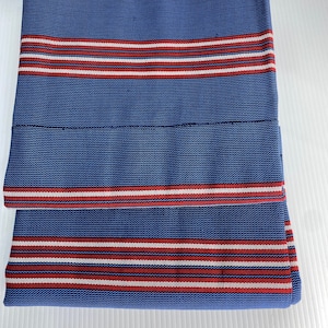 May include: A blue and white fabric with red stripes. The fabric is folded in half and is lying on a white surface.