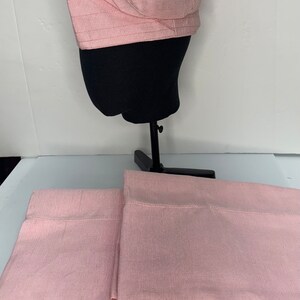 May include: Two pink flat sheets with a subtle ribbed texture. A pink fabric hat is displayed on a black mannequin head.