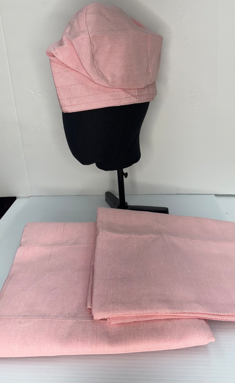 May include: Two pink flat sheets with a subtle ribbed texture. A pink fabric hat is displayed on a black mannequin head.