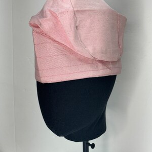May include: A pink bucket hat with a wide brim and a slightly curved crown. The hat is made of a soft, textured fabric.