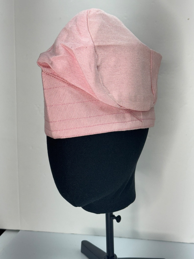May include: A pink bucket hat with a wide brim and a slightly curved crown. The hat is made of a soft, textured fabric.