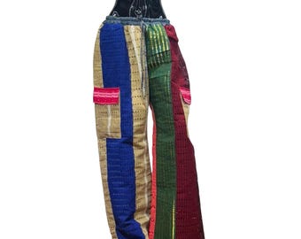 Puede incluir: Pantalones de patchwork coloridos con cintura con cordón. Los pantalones presentan una mezcla de paneles azules, beige, verdes y rojos con un diseño texturizado y perforado. Se ven dos bolsillos, uno rosa y otro rojo.