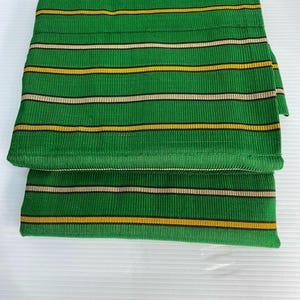 Puede incluir: Tela rayada verde y dorada doblada por la mitad. La tela tiene una textura tejida.