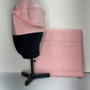 May include: A pink fabric hat with a wide brim and a matching fabric rectangle. The hat is on a black stand.