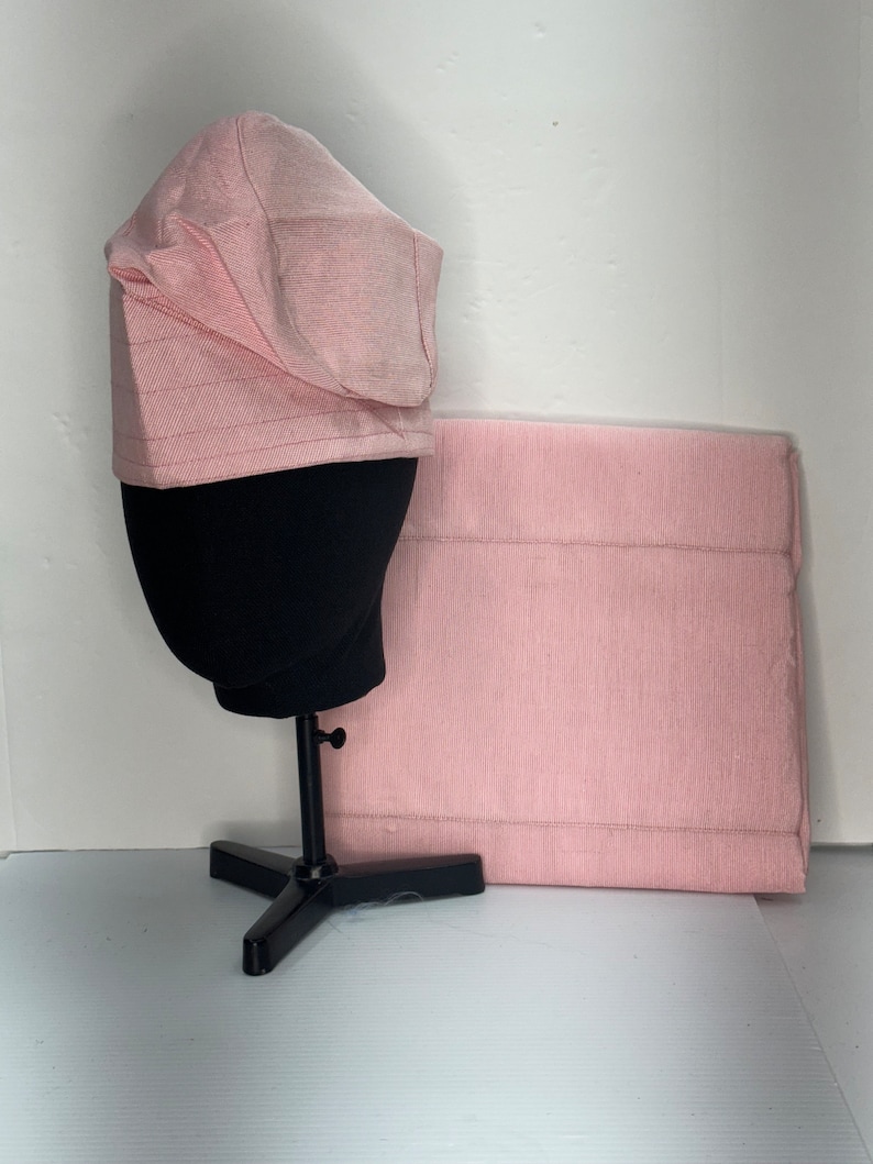 May include: A pink fabric hat with a wide brim and a matching fabric rectangle. The hat is on a black stand.