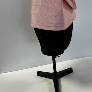 May include: A pink fabric hat with a textured pattern. The hat is on a black mannequin head.