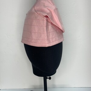 May include: A pink, patterned fabric hat with a pointed top. The hat is on a black mannequin head.