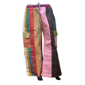 Op de afbeelding: Kleurrijke broek met wijde pijpen en een patchwork-ontwerp. De broek heeft verticale strepen in verschillende kleuren, waaronder roze, bruin, groen en geel. Het heeft twee zakken en een tailleband met trekkoord. De stof is lichtgewicht.