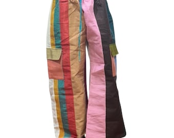 May include: Colorful, wide-leg pants with a patchwork design. The pants feature vertical stripes in various colors, including pink, brown, green, and yellow. They have two pockets and a drawstring waist. The pants are made of a lightweight fabric.