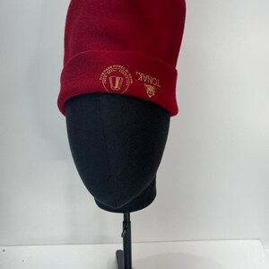 May include: A red fleece beanie with a gold embroidered logo that says "TONAK" and "MADE IN CZECH REPUBLIC".