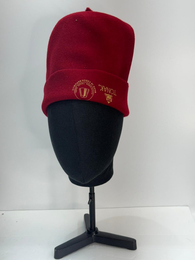 May include: A red fleece beanie with a gold embroidered logo that says "TONAK" and "MADE IN CZECH REPUBLIC".