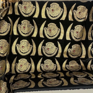 Puede incluir: Tela de terciopelo negro con un patr&oacute;n repetido de cabezas de le&oacute;n doradas. Los leones est&aacute;n rodeados por una forma de media luna dorada.