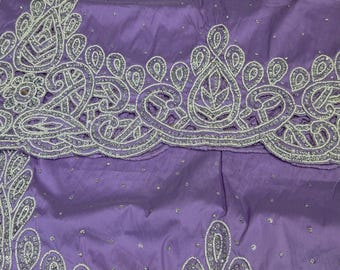 Puede incluir: Una tela de color lavanda con intrincados bordados plateados y abalorios en patrones de cachemira y florales. El diseño incluye un borde ancho festoneado con detalles de hilo metálico denso y pequeñas cuentas plateadas dispersas.