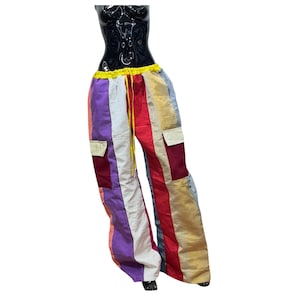 May include: Colorful, striped pants with a drawstring waist and two cargo pockets. The pants feature vertical stripes in various colors, including purple, red, gold, and white. The waistband is yellow, and the drawstring is yellow.