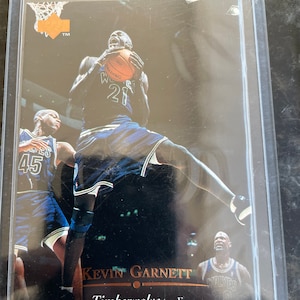 May include: A basketball trading card featuring Kevin Garnett of the Minnesota Timberwolves. The card is a close-up of Garnett in action, wearing his team's jersey with the number 21. The card has a gold border and the text "Kevin Garnett" and "Timberwolves - F" on the bottom.