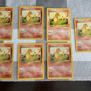 May include: Six yellow Pokemon trading cards featuring the character Charmander. Each card has a picture of Charmander, the name "Charmander" at the top, and the text "Scratch" and "Ember" with their corresponding attack points.