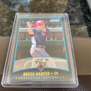 Puede incluir: Una tarjeta de béisbol con Bryce Harper, un jardinero de los Washington Nationals. La tarjeta es una tarjeta cromada y presenta una foto de Harper con su uniforme, balanceando un bate. La tarjeta también incluye la firma de Harper y el número 31.