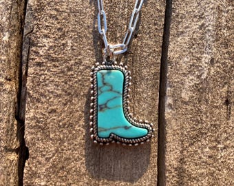 Könnte beinhalten: Silberne Halskette mit einem Anhänger in Form eines Cowboy-Stiefels. Der türkisfarbene Anhänger hat braune Adern und einen silberfarbenen Rand. Die Kette ist eine silberfarbene Gliederkette.