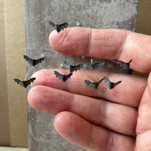 以下が含まれることがあります： 薄く透明で湾曲したプラスチックワイヤーに取り付けられた、7つの黒いコウモリのミニチュアフィギュアのコレクション。小さく詳細なコウモリのフィギュアは散らばった状態で配置されており、その翼幅と質感のある体を見せています。