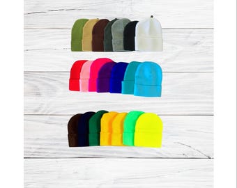 May include: A collection of colorful beanies in various shades, including green, brown, black, white, pink, purple, blue, teal, yellow, and neon green. The beanies are arranged in rows, showcasing a variety of colors.