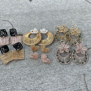 Puede incluir: Surtido de pendientes de alambre hechos a mano en varios estilos. Los pendientes presentan alambre dorado, plateado y negro con detalles de perlas y cristales. Los pendientes se muestran sobre una superficie gris.
