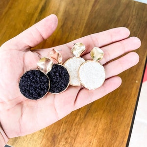 Puede incluir: Un par de pendientes de tono dorado con abalorios redondos de color negro y blanco. Los pendientes tienen un diseño simple y moderno.