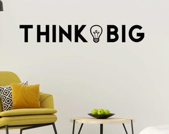 May include: A black wall decal featuring the text THINK BIG, where the letter I is replaced by a line-art lightbulb icon. The lettering is bold, sans-serif, and uppercase, applied directly to a plain white wall surface above a yellow armchair.