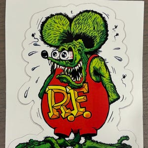May include: A sticker featuring a cartoon rat with green fur and large ears. The rat wears a red outfit with the letters "R.E." in yellow. The rat has an angry expression with wide eyes and sharp teeth.