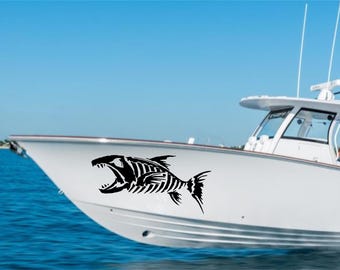 May include: A black fish skeleton decal is affixed to the side of a white boat. The boat is on the water with a blue sky in the background. The fish skeleton has an open mouth and detailed bone structure.