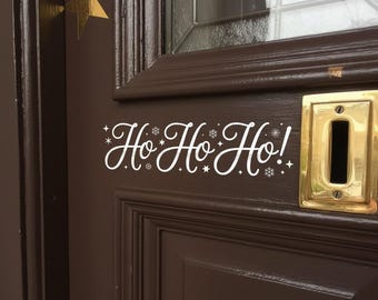 May include: A brown wooden door with a gold star and snowflake decals. The door features a brass mail slot and the text "Ho Ho Ho!" in white script, decorated with snowflakes and stars, perfect for the holiday season.